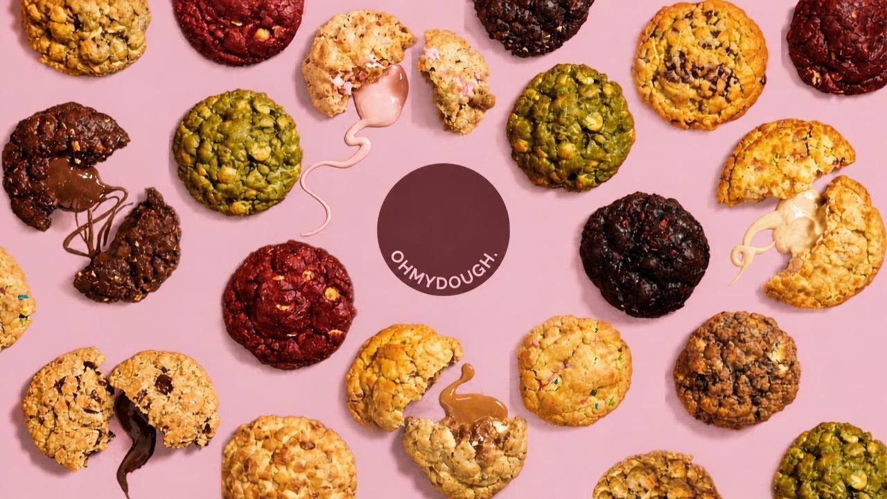 An assortment of Oh My Dough gourmet cookies on a pink background